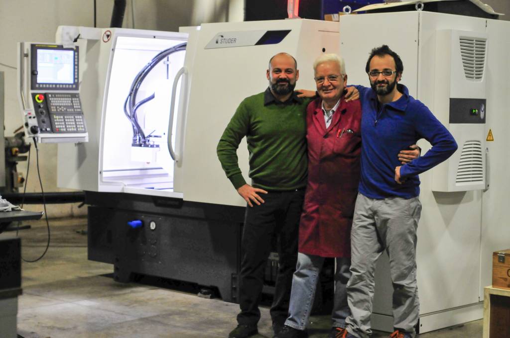 The company's three founders pose in the workshop, in front of a modern Studer grinding machine.